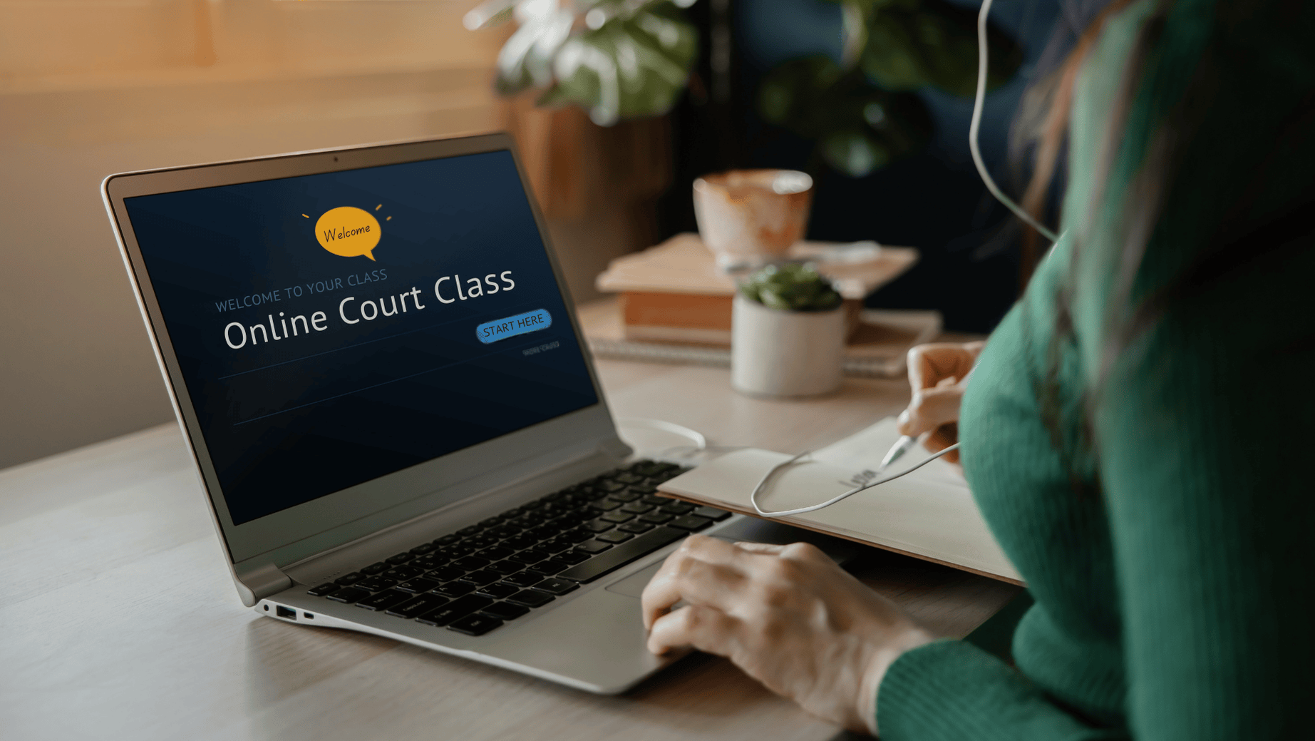 Person taking online court class on laptop, writing notes while wearing headphones, screen displaying Online Court Class welcome.